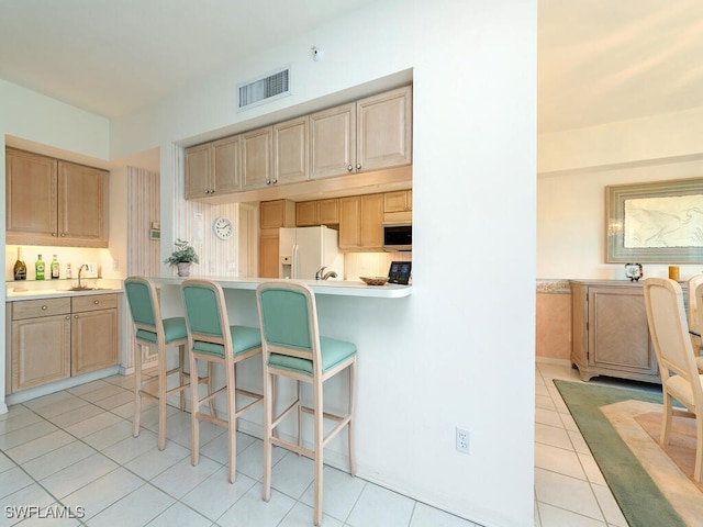 kitchen with light tile patterned flooring, light brown cabinetry, and white fridge with ice dispenser