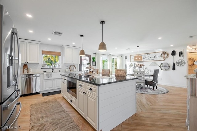 kitchen featuring pendant lighting, light parquet floors, stainless steel appliances, a center island, and white cabinets