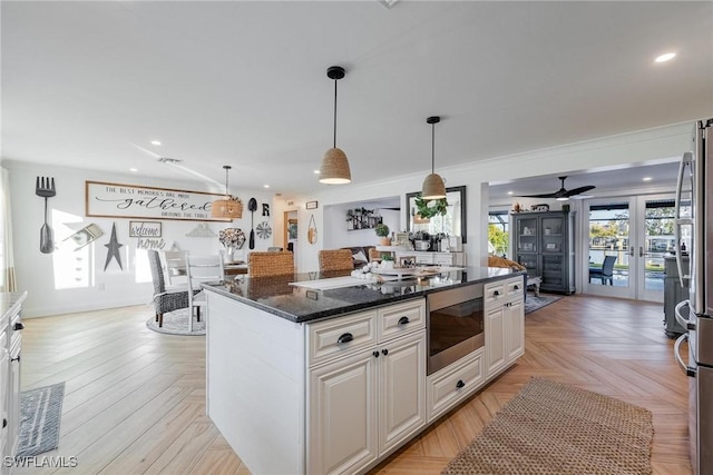 kitchen with built in microwave, a center island, dark stone counters, light parquet flooring, and white cabinets