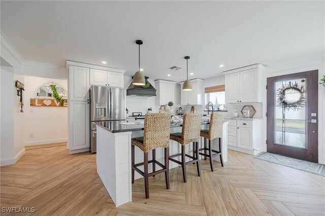 kitchen with stainless steel refrigerator with ice dispenser, white cabinetry, a kitchen island, and premium range hood