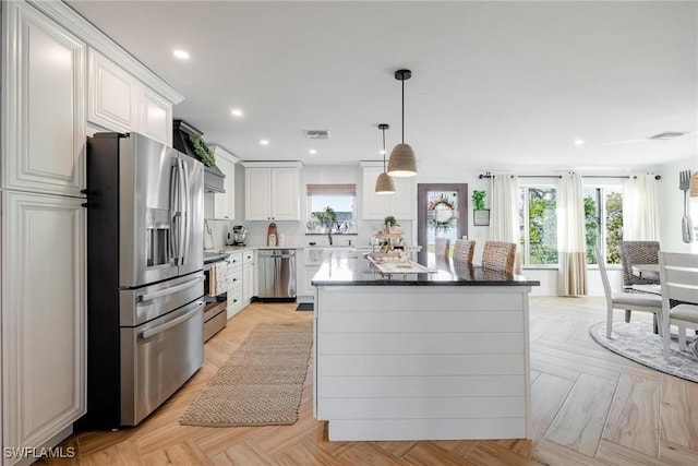 kitchen featuring appliances with stainless steel finishes, pendant lighting, white cabinets, light parquet floors, and a center island