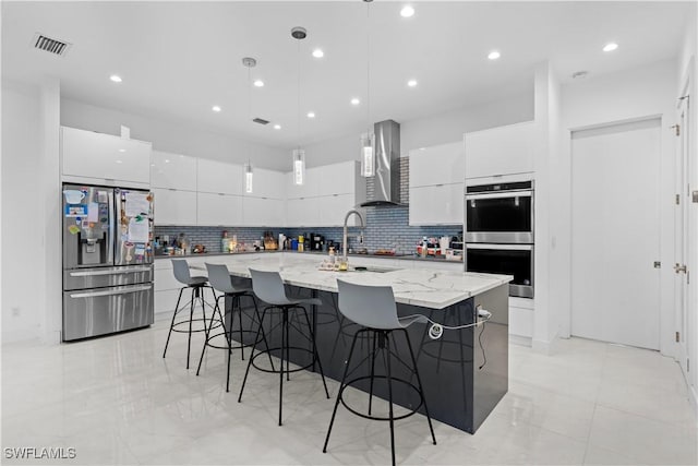 kitchen with a large island, appliances with stainless steel finishes, white cabinetry, decorative light fixtures, and wall chimney exhaust hood