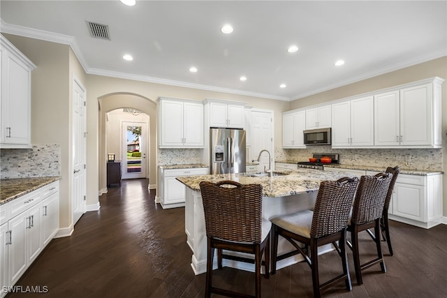 kitchen with appliances with stainless steel finishes, white cabinetry, sink, a kitchen island with sink, and light stone counters