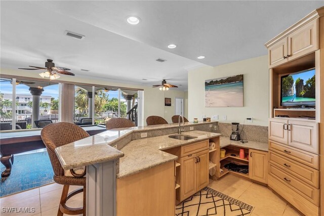 kitchen featuring a breakfast bar, sink, light tile patterned floors, light stone counters, and light brown cabinets