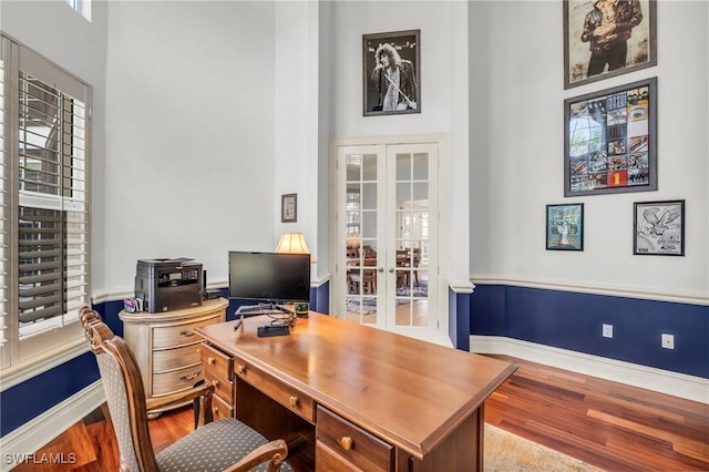 office space featuring french doors, a towering ceiling, and hardwood / wood-style floors