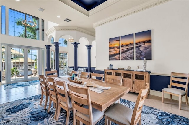 tiled dining room with crown molding, decorative columns, french doors, and a high ceiling