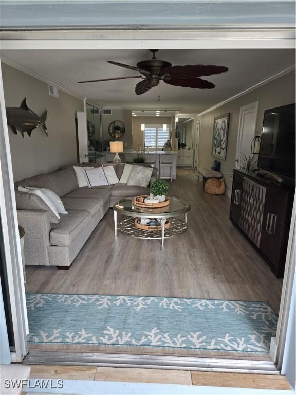 living room featuring ornamental molding, wood-type flooring, and ceiling fan