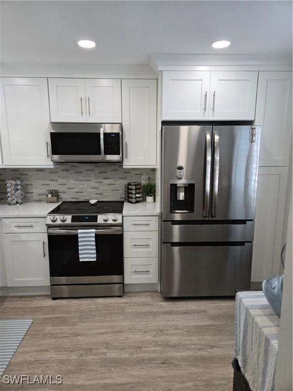 kitchen with appliances with stainless steel finishes, backsplash, white cabinets, and light hardwood / wood-style floors