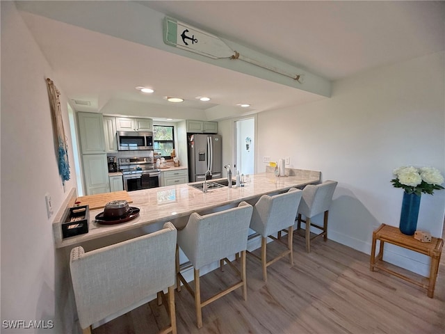 kitchen featuring appliances with stainless steel finishes, a breakfast bar, sink, kitchen peninsula, and light wood-type flooring