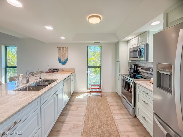 kitchen with sink, backsplash, stainless steel appliances, light stone countertops, and light wood-type flooring