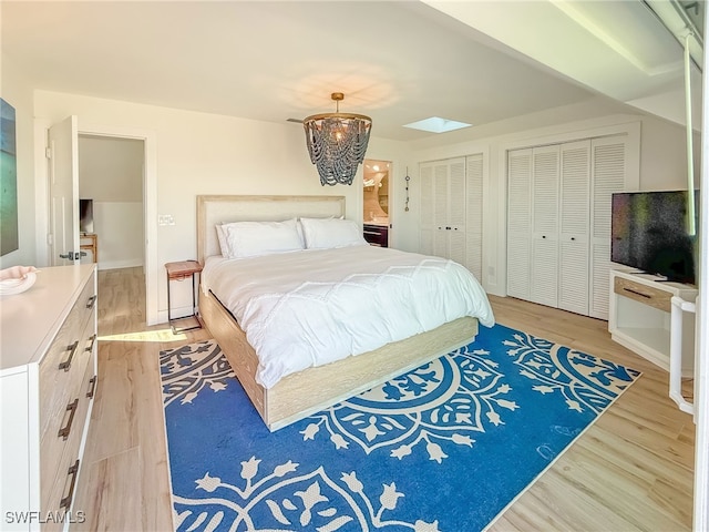 bedroom featuring multiple closets, a skylight, and light hardwood / wood-style flooring