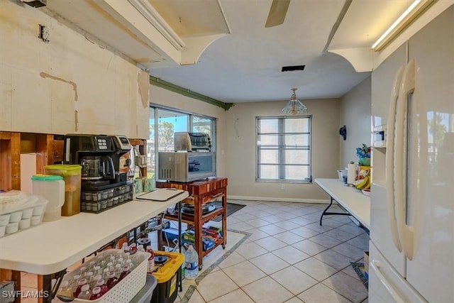 kitchen with light tile patterned flooring, decorative light fixtures, white refrigerator with ice dispenser, and a wealth of natural light