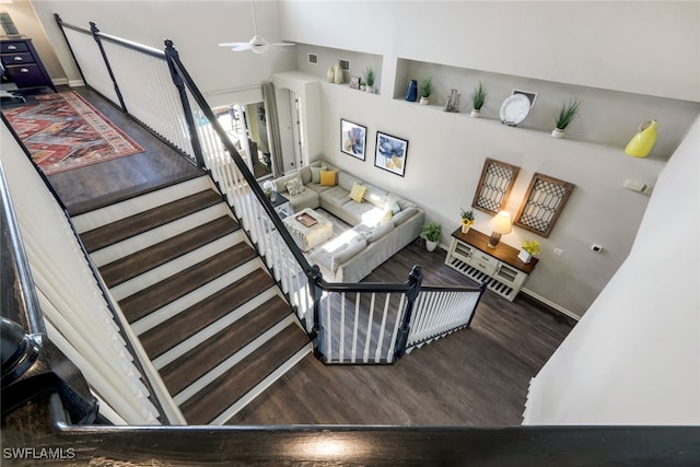 staircase with wood finished floors, ceiling fan, and baseboards