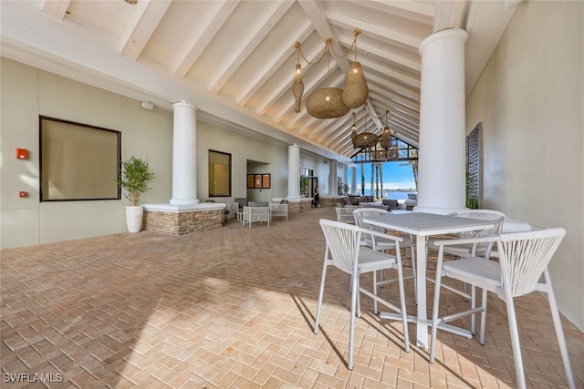 interior space featuring decorative columns, high vaulted ceiling, brick floor, and beam ceiling