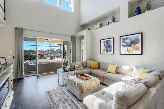 living room featuring dark wood-type flooring, a high ceiling, and ceiling fan