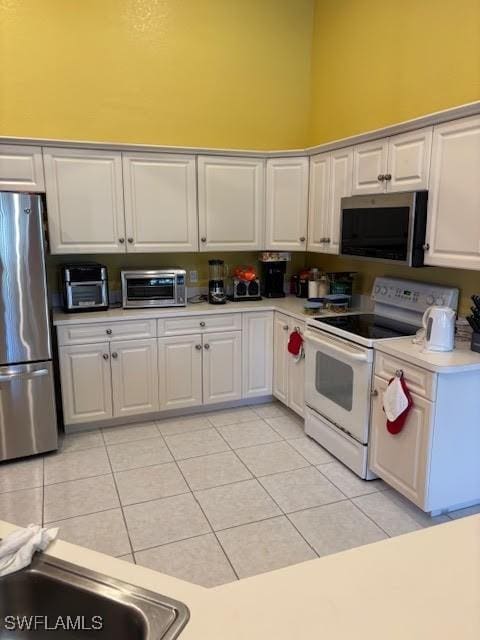 kitchen featuring white cabinetry, light tile patterned floors, a towering ceiling, and appliances with stainless steel finishes