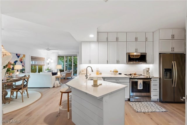 kitchen with appliances with stainless steel finishes, white cabinetry, sink, a kitchen bar, and kitchen peninsula