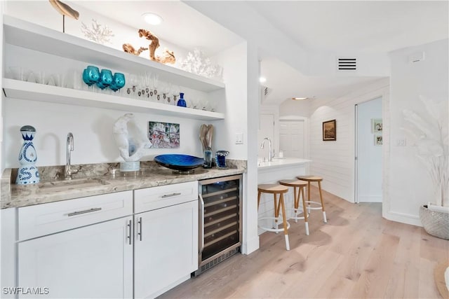 bar featuring wine cooler, sink, light wood-type flooring, light stone countertops, and white cabinets