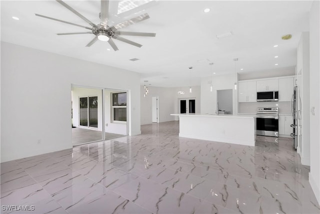 interior space featuring ceiling fan, hanging light fixtures, stainless steel appliances, white cabinets, and a kitchen island