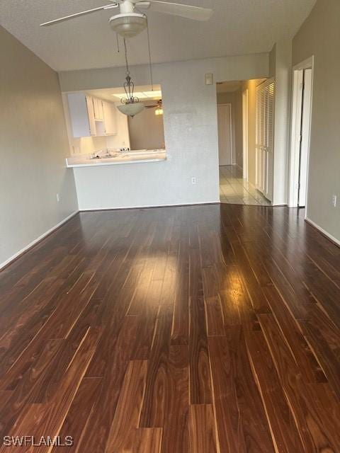 unfurnished living room featuring baseboards, dark wood-style flooring, and ceiling fan