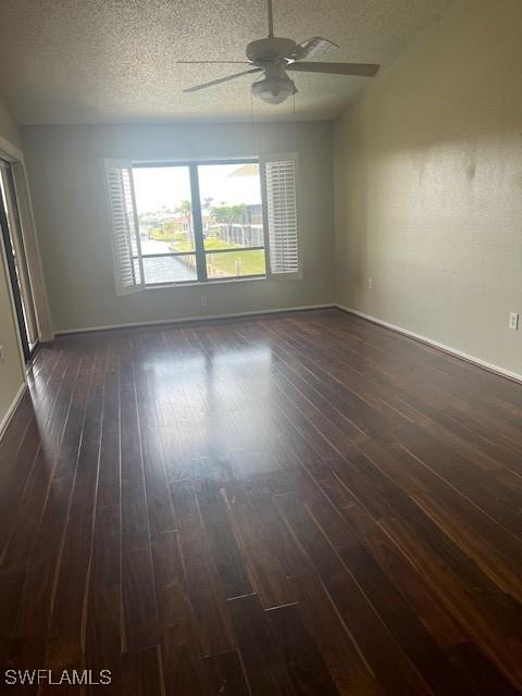 spare room featuring baseboards, a textured ceiling, dark wood-style floors, and a ceiling fan