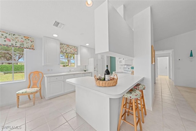 kitchen featuring white appliances, visible vents, a breakfast bar, light countertops, and white cabinetry