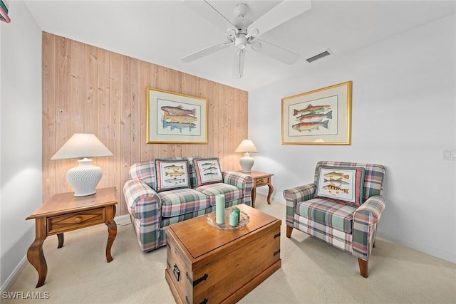 carpeted living room with wood walls, baseboards, visible vents, and a ceiling fan