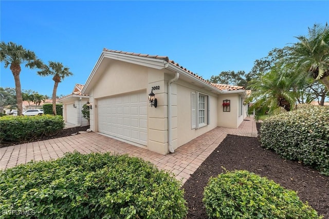 view of home's exterior with an attached garage, driveway, a tile roof, and stucco siding