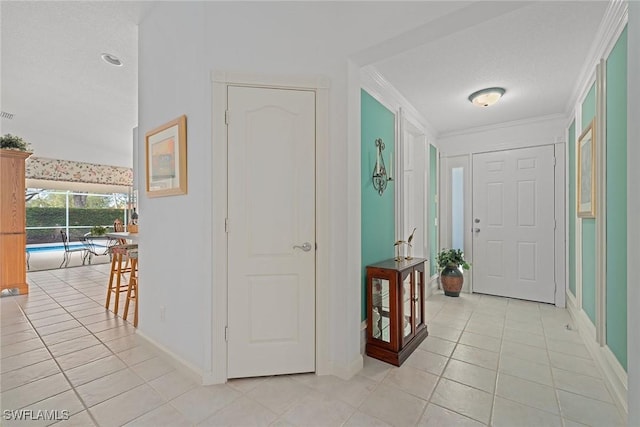 foyer with a textured ceiling, baseboards, crown molding, and light tile patterned flooring