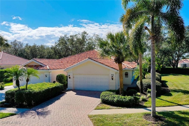 mediterranean / spanish-style house with a garage, decorative driveway, a tile roof, and stucco siding