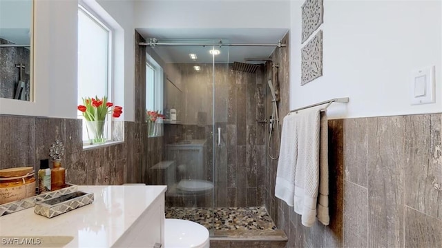 bathroom with a shower with door, vanity, tile walls, and toilet