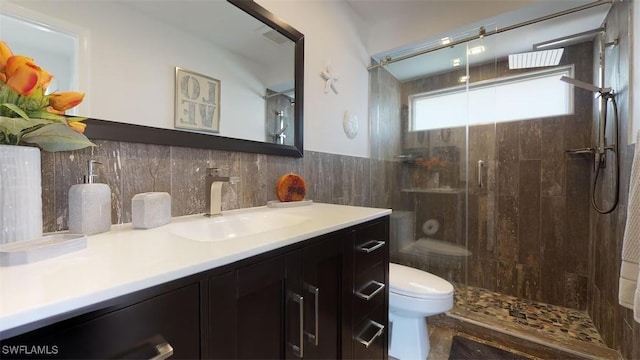 bathroom featuring a tile shower, vanity, tile walls, and toilet