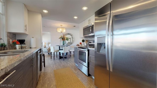 kitchen with white cabinetry, pendant lighting, light hardwood / wood-style floors, and appliances with stainless steel finishes