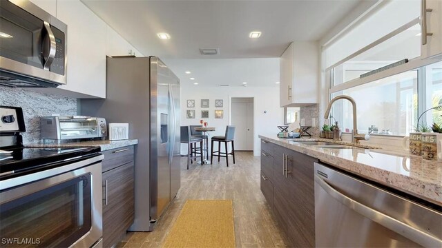 kitchen with sink, dark brown cabinets, stainless steel appliances, light stone countertops, and white cabinets