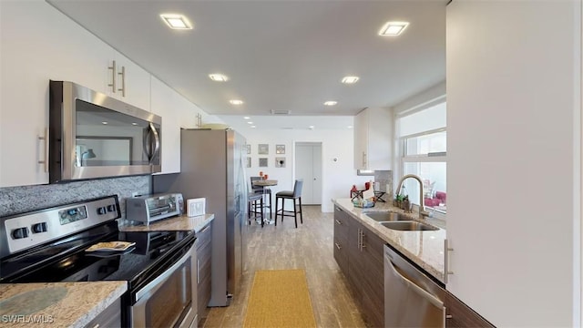 kitchen featuring white cabinetry, sink, light stone countertops, and appliances with stainless steel finishes