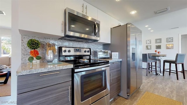 kitchen with white cabinetry, light stone counters, light wood-type flooring, stainless steel appliances, and backsplash