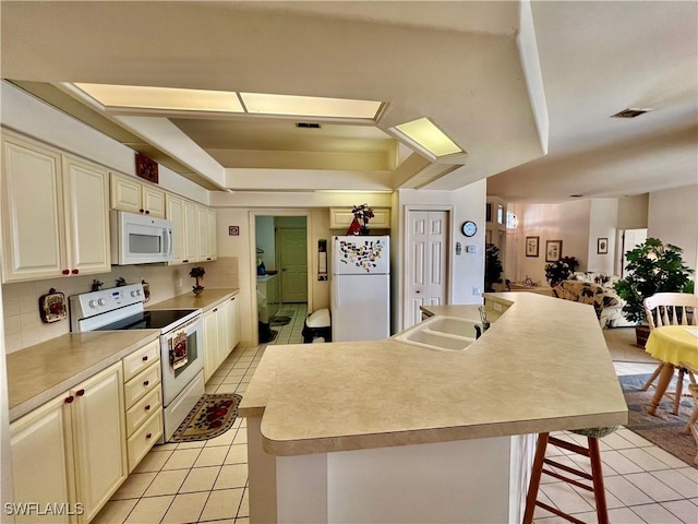 kitchen featuring a tray ceiling, light tile patterned floors, decorative backsplash, a sink, and white appliances