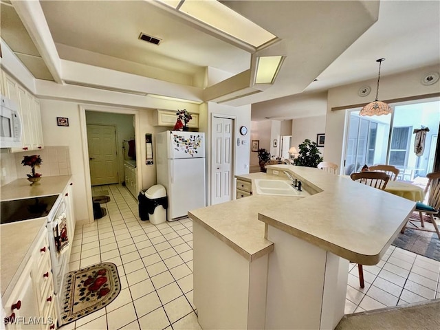 kitchen featuring a breakfast bar area, light countertops, open floor plan, a sink, and white appliances