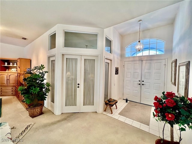 entryway featuring light tile patterned floors, visible vents, a towering ceiling, an inviting chandelier, and light carpet