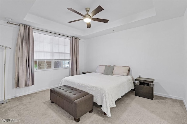 bedroom with a raised ceiling, light carpet, and ceiling fan