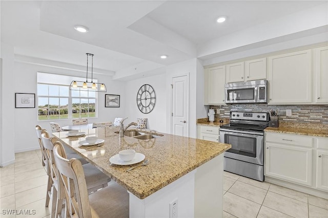 kitchen featuring decorative light fixtures, light stone counters, a tray ceiling, stainless steel appliances, and a center island with sink