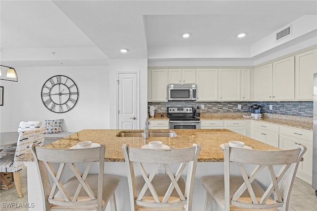 kitchen featuring light stone counters, appliances with stainless steel finishes, a kitchen bar, and sink