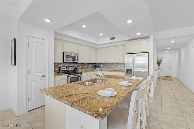 kitchen featuring a kitchen bar, sink, light stone counters, appliances with stainless steel finishes, and an island with sink