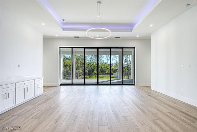 empty room with a wealth of natural light, light wood-type flooring, and a tray ceiling