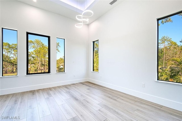 unfurnished room featuring an inviting chandelier, a high ceiling, and light wood-type flooring