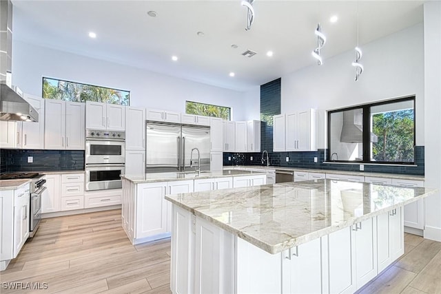 kitchen with light hardwood / wood-style flooring, high quality appliances, light stone counters, an island with sink, and white cabinets