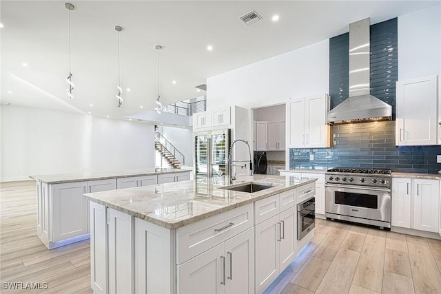 kitchen with an island with sink, sink, stainless steel stove, and wall chimney exhaust hood