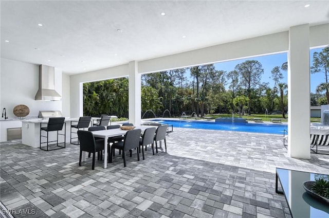 pool with outdoor dining space, outdoor wet bar, exterior kitchen, a sink, and a patio area