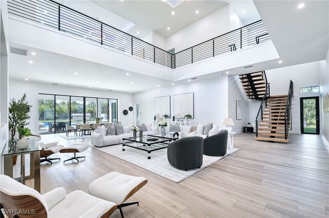 living room with visible vents, wood finished floors, recessed lighting, stairway, and a towering ceiling