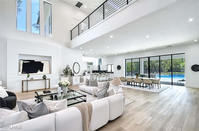 living room with recessed lighting, light wood-type flooring, baseboards, and a towering ceiling